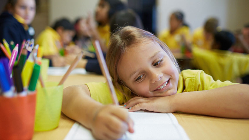 A girl smiles as she writes with pencil on paper