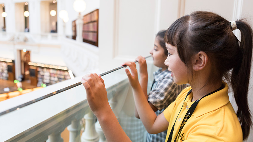 schoolgirls peering over the ornate balcony of a Dome Gallery in the octagonal La Trobe Reading Room