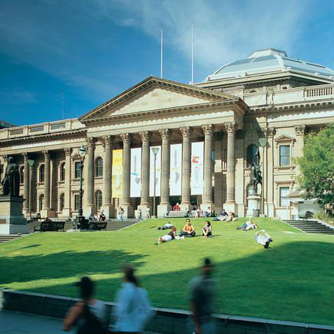 portico and facade of State Library Victoria with green grass and blue sky