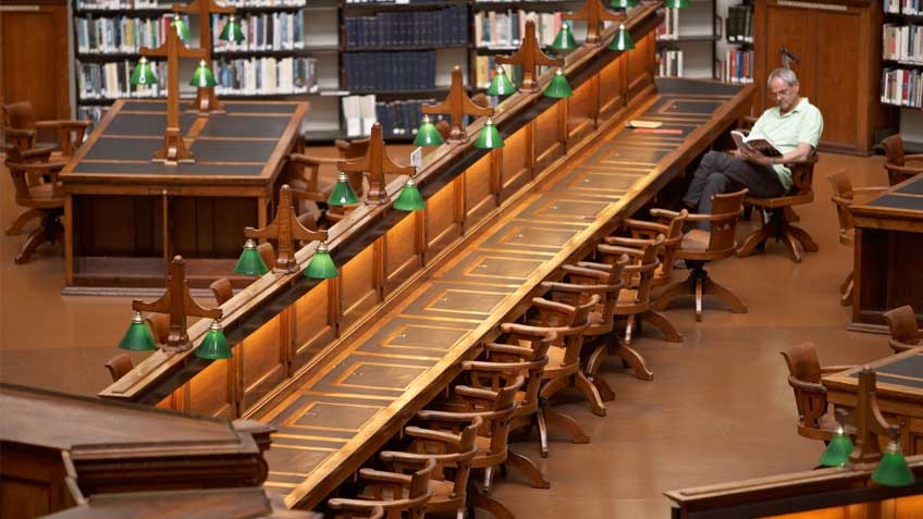A man reads a book at a heritage desk in the La Trobe Reading Room
