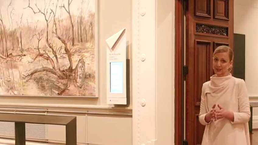 A woman in a white dress stand beside a painting of a scorched landscape