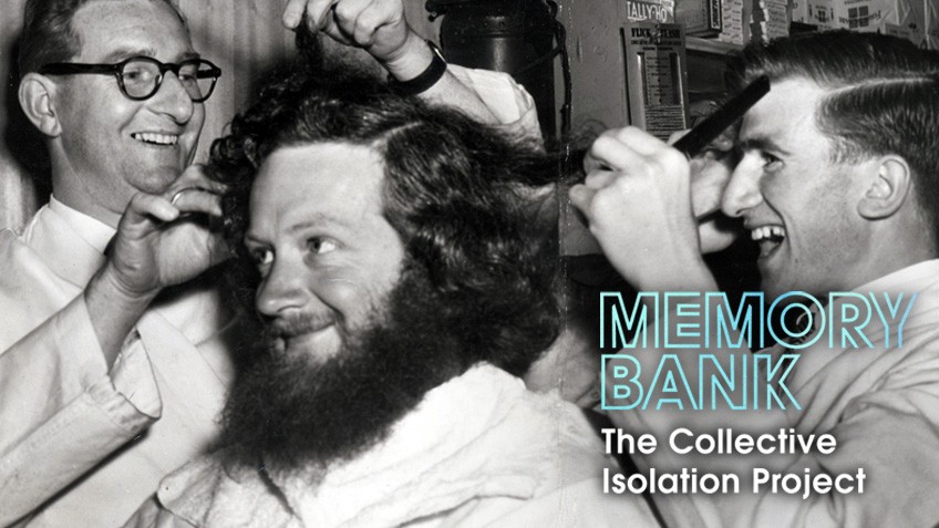 A man with a big beard and hair receives a trim while three other men look on smiling