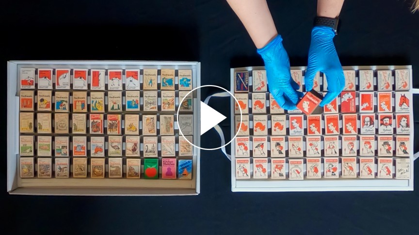 Two boxes full of small matchboxes, and gloved hands picking one up