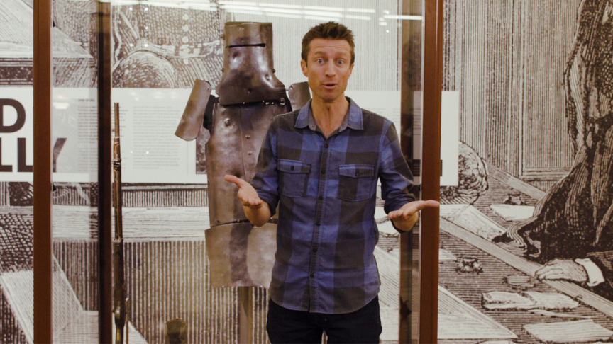 Sammy J standing in front of Ned Kelly's armour at State Library Victoria